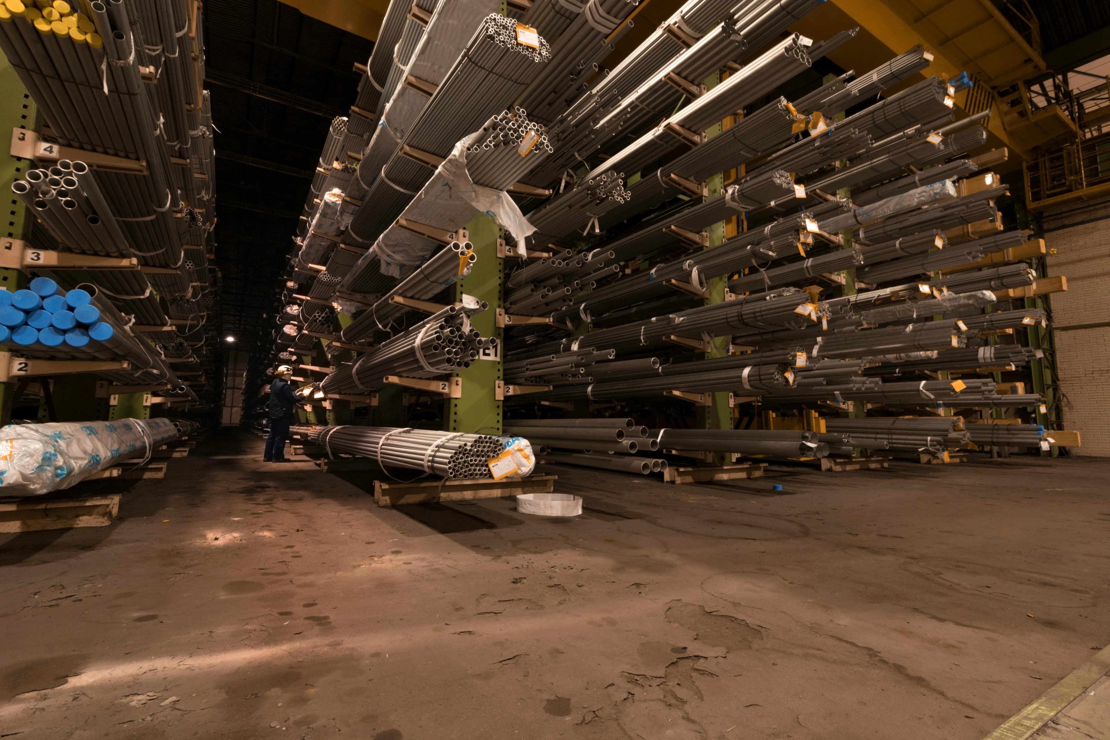 Stacks of clean aluminium extrusion in a UK scrap yard with industrial cranes and storage bays in the background